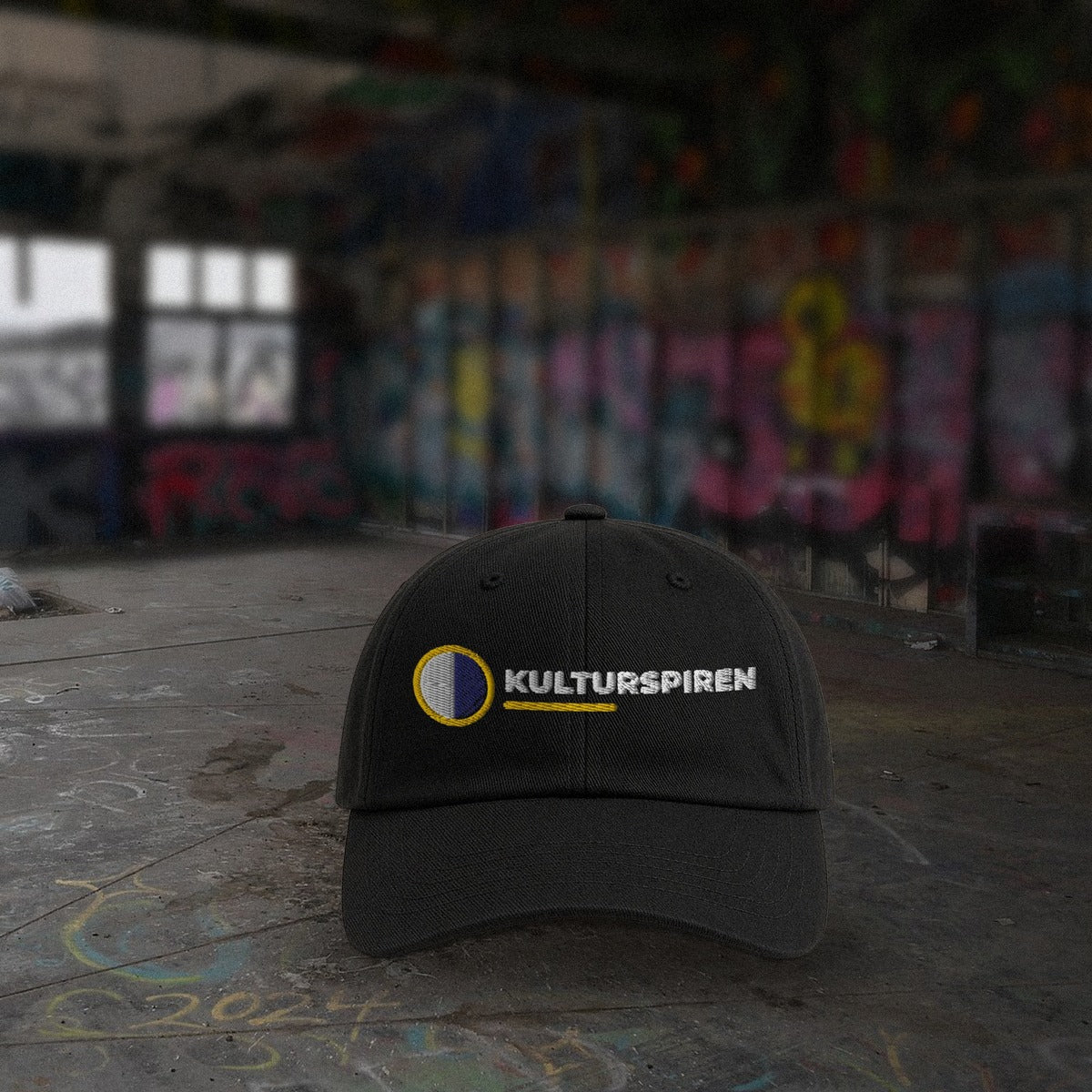 Svart Kulturspiren-kaps på betonggulv foran graffitivegger